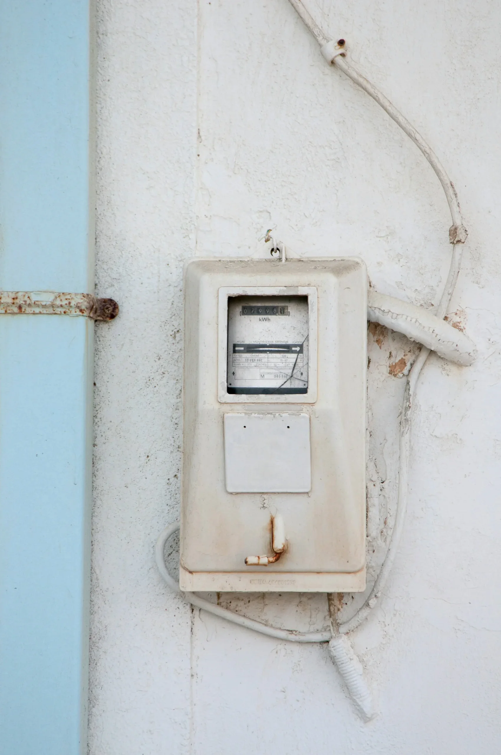 An old-fashioned white electric meter mounted on a grayish-white wall, representing electricity bill management