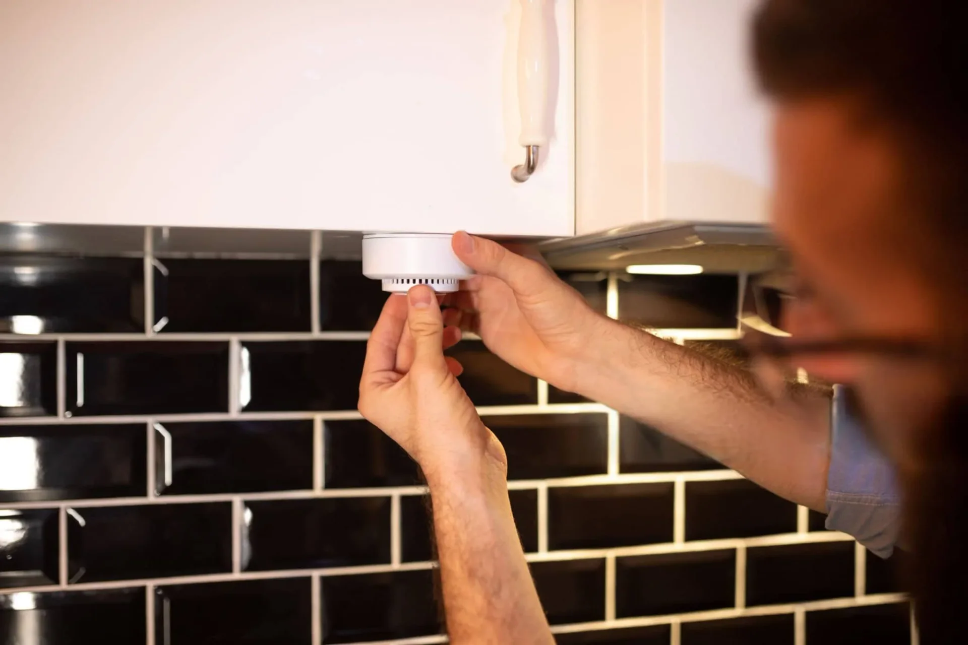 homeowner testing carbon monoxide alarm to detect gas leak in modern kitchen for home safety