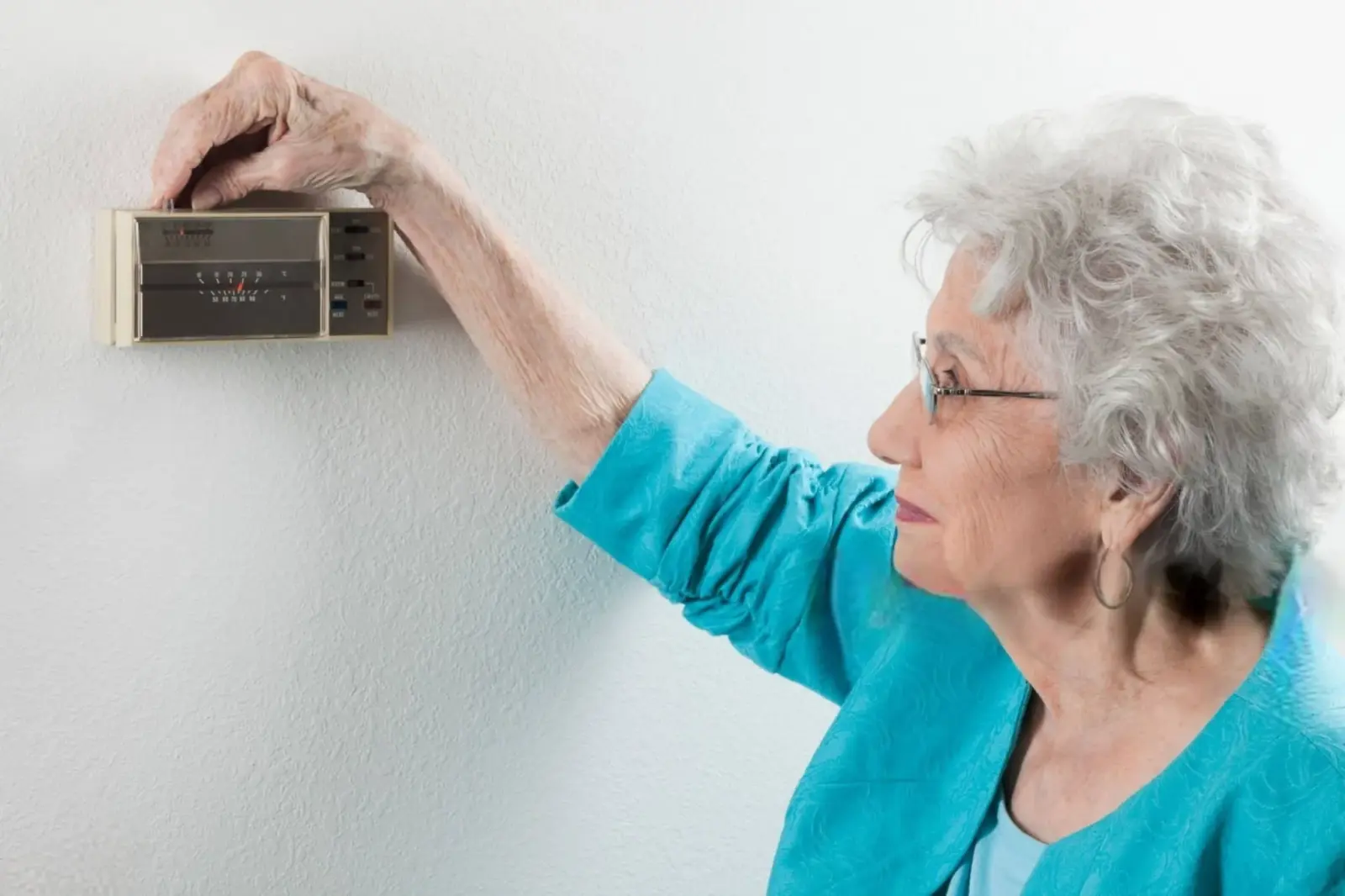 Best Thermostat for Heat Pump in 2024: Compare WiFi, Programmable & Smart Options 1 A old woman Adjusting The Thermostat At Home -