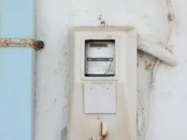 An old-fashioned white electric meter mounted on a grayish-white wall, representing electricity bill management