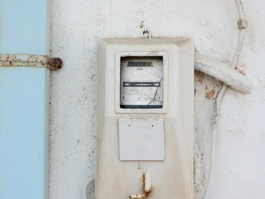 An old-fashioned white electric meter mounted on a grayish-white wall, representing electricity bill management